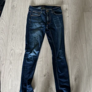 Mörkblå jeans från Nudie Jeans Co - Snygga mörkblå jeans från Nudie Jeans Co med klassisk femficksdesign och kontrastsömmar. Jeansen har en rak passform och är tillverkade i slitstarkt bomullsjeans. Perfekta för dig som gillar en tidlös och stilren look.
