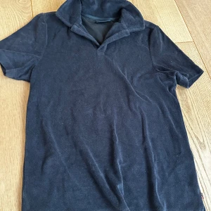 Mörkblå frotté t-shirt från Lexington - Snygg mörkblå t-shirt från Lexington i mjuk frotté. Klassisk krage och korta ärmar ger en chill och sportig vibe. Perfekt för dig som gillar stilrena och bekväma plagg med lite extra känsla.