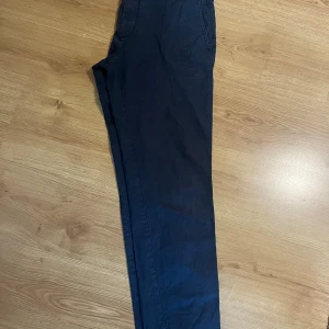 Mörkblå chinos från Hugo Boss - Snygga mörkblå chinos från Hugo Boss med regular fit och stretch för extra komfort. Byxorna har klassiska fickor fram och bak, samt diskret knappdetalj bak. Perfekta för en clean och stilren look.