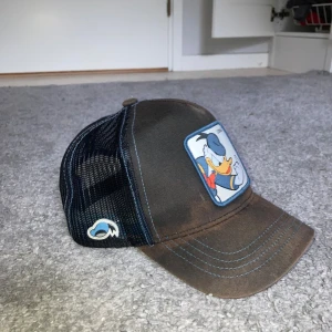 Capslab keps med Kalle Anka-motiv - Snygg keps från Capslab med Kalle Anka-tryck framtill. Kepsen är svart med blå sömmar och har mesh-bakstycke för extra ventilation. Justerbar snapback baktill och broderad detalj på sidan. Perfekt för dig som gillar Disney och streetstyle. Kepsen är dock ganska solblekt men tycker själv att den inte blir ful för det, tycker det blir ganska snyggt.