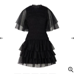 By malina volangklänning  - Supersnygg By Malina Minnie-klänning, en svart kort modell med flera lager volanger och transparenta meshärmar. Klänningen har en rund hals och är tillverkad i ett lätt, luftigt material som ger en cool och trendig look. Perfekt för dig som vill sticka ut med en unik stil. Klänningen är använd endast en gång.