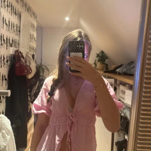 Rosa randig kortklänning från Zara - Supersöt rosa och vit randig tröja  från Zara med knytning framtill och puffiga korta ärmar. Lätt och luftig modell i bomull, perfekt för varma dagar. Snygg v-ringning och avslappnad passform som ger en chill vibe.