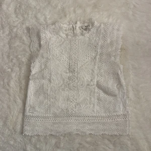 Vit spetsblus från ONLY - Superfin vit blus från ONLY i spets med vackra broderade detaljer och vågiga kanter. Ärmlös modell med hög hals och knäppning bak. Perfekt för dig som gillar romantisk och feminin stil. Tröjan är helt oanvänd och har pris lapp på i storlek S, hör av er för fler bilder!