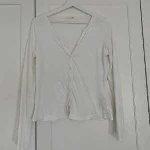 Vit Odd Molly blus med knappar - Säljer en vit blus från Odd Molly med v-ringning och dekorativa knappar framtill. Toppen har långa ärmar och är tillverkad i mjuk bomull. Enkel och stilren design med lätt rynk vid midjan för en snygg passform.