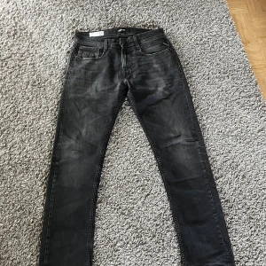 Replay Rocco svarta jeans, storlek 29/31 - Svarta Replay Rocco jeans i comfort fit med klassisk femficksdesign. Jeansen har en lätt tvättad look och raka ben. Snygga detaljer med Replay-logga på fickan och robust knappstängning. Perfekta för dig som gillar en avslappnad men stilren vibe.
