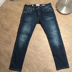 Replay Anbass slim jeans blå 33/30 - Snygga mörkblå Replay Anbass jeans i slim fit med klassisk femficksdesign och snygga slitningar. Jeansen har normal midja och raka ben, tillverkade i stretchig denim för skön passform. Perfekta för dig som gillar stilrena och moderna jeans. Ny pris 1800, mitt pris 1200. Kan säljas billigare vid snabb affär. 