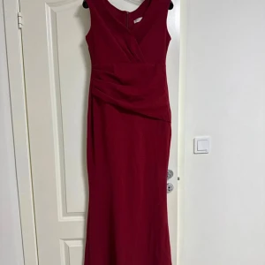 Vinröd långklänning med omlott - Snygg vinröd långklänning med omlott-detalj upptill och drapering i midjan. Ärmlös modell med v-ringning och dragkedja bak. Perfekt för dig som vill sticka ut med en elegant och stilren look. Från bubbleroom, goddiva