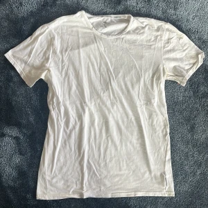 Vit t-shirt från Calvin Klein - En klassisk vit t-shirt från Calvin Klein i mjuk bomull. T-shirten har rund halsringning, korta ärmar och diskret logga på insidan av kragen. Perfekt basic-plagg att ha i garderoben.