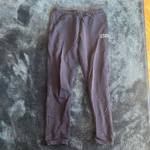 Mörklila mjukisbyxor från Frank Dandy - Mörklila mjukisbyxor från Frank Dandy i 100% bomull. Byxorna har resår och snörning i midjan, sidofickor och en bakficka. Diskret logga framtill och smal passform med muddar vid bensluten. Perfekta för chill eller träning.