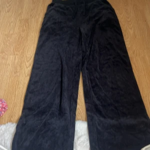 Svarta vida mjukisbyxor i sammet - Mysiga svarta mjukisbyxor i sammet med bred resår och snörning i midjan. Byxorna har en loose och wide passform som ger en avslappnad vibe. Perfekta för chill dagar hemma eller när du vill vara extra bekväm.