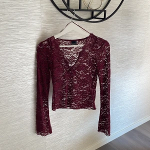 Vinröd spetsblus från Gina XS - Säljer en vinröd blus i spets från Gina Tricot i storlek XS. Blusen har långärmade ärmar, v-ringad hals och är genombruten med blommigt spetsmönster. Modellen är slim passform som sitter snyggt på kroppen.