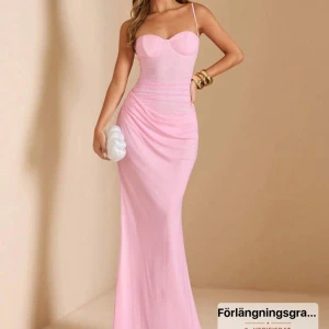 Ljusrosa långklänning med smala axelband - Supersnygg ljusrosa långklänning med figurnära passform och smala axelband. Klänningen har en markerad byst och lätt drapering över höfterna för en elegant siluett. Perfekt för dig som vill sticka ut med en feminin och stilren look.