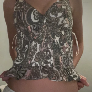 Paisleymönstrad topp från Missguided - Paisleymönstrad linnetopp från Missguided i beige, rosa och grå toner. Toppen har smala axelband, v-ringning, smockad midja och volangkant nertill. Snygg croppad. Aldrig använd!! 