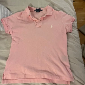 Rosa pikétröja från Ralph Lauren - Säljer en klassisk söt rosa pikétröja från Ralph Lauren i modellen The Skinny Polo. Tröjan har korta ärmar, krage med knappar och den ikoniska broderade loggan på bröstet! Sitter väldigt bra och är i storlek M men passar även bra på S och Xs💞Hör av er om ni vill diskutera pris💖