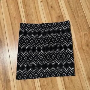 Svartvit mönstrad kortkjol - Säljer en svartvit kortkjol med grafiskt zigzag- och diamantmönster. Kjolen har rak passform och är perfekt för dig som gillar att sticka ut med coola mönster. Materialet känns som bomull eller polyester och kjolen är lätt att matcha med både enkla och färgstarka toppar.