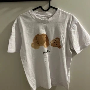 Vit Palm Angels t-shirt med nalletryck - Nu säljer jag min vita Palm angels tröja som är i bra skick nästan oanvänd. De är inga taggar eller något men texten och björnen ser bra ut. Tveka inte och skicka om ni undrar något och priset är inte hugget i sten!