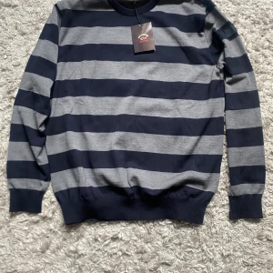 Randig tröja från Paul & Shark - Säljer en snygg långärmad tröja från Paul & Shark i marinblått och grått med breda ränder. Tröjan har rund halsringning och ribbade muddar. Perfekt för dig som gillar klassisk stil med en sportig touch. Nypriset är ca 3000