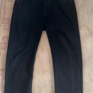 Svarta jeans från Emporio Armani - Svarta jeans från Emporio Armani med klassisk femficksdesign och diskret broderad logga på bakfickan. Jeansen har rak passform och är tillverkade i ett mjukt bomullsmaterial med stretch för extra komfort. Snygg läderpatch med logga i midjan.