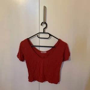 Röd croppad topp Jumpee & Punnee - Croppad röd topp från Jumpee & Punnee med korta ärmar och djup v-ringning. T-shirten har en enkel design och är tillverkad i mjuk bomull, perfekt för en avslappnad och trendig look.