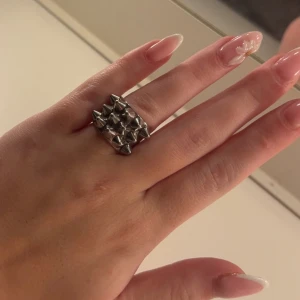 Silvrig ring med nitar från Edblad - Cool och edgy ring från Edblad i silvrig metall med flera konformade nitar som ger en riktigt tuff vibe. Perfekt för dig som vill sticka ut och addera lite attityd till din stil. Ringen är bred och har en rejäl känsla.