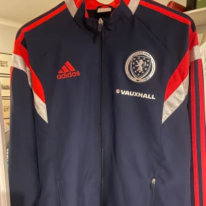 Adidas Scotland träningsjacka M - Mörkblå träningsjacka från Adidas med röda och silvriga detaljer, dragkedja framtill och broderad Scotland-logga på bröstet. Vintage/retro stil