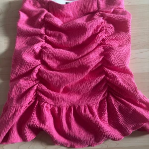 Rosa volangkjol från Gina Tricot XS - Supersöt kortkjol från Gina Tricot i en stark rosa färg. Kjolen har volangkant nertill och snygga rynkade detaljer framtill. Tillverkad i ett strukturerat, stretchigt tyg som sitter bekvämt och ger en cool look.