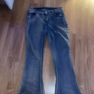 Blå bootcut jeans med fickdetaljer - Snygga blå jeans med bootcut passform och klassisk femficksdesign. Jeansen har en cool tvättad look och markerade sömmar, samt fickor med lock och knapp bak. Perfekta för dig som gillar en retrostil med lite extra vidd nertill.