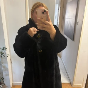 Svart pälsjacka - Säljer en svart pälsjacka i syntetmaterial. Jackan har en rak och rymlig passform med lång ärm och hög krage. Perfekt för dig som vill ha en statementjacka med lyxig känsla och cool look. Den översta ”ögglan” har lossnat i en söm lätt åtgärdat annars helt felfri 
