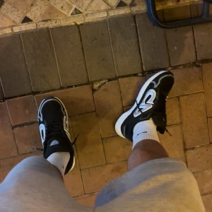 Svarta och vita Nike sneakers - Säljer ett par svarta och vita Nike sneakers med snygg, sportig design och tydliga vita detaljer på sidorna. Skorna har snörning och en tjock, vit sula som ger en modern look. Perfekta för dig som gillar streetstyle och vill sticka ut med dina skor.