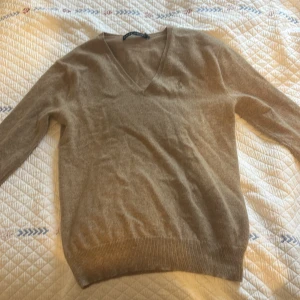 Beige v-ringad kashmirtröja Ralph Lauren - Supermjuk beige v-ringad tröja från Ralph Lauren i lyxig kashmir. Klassisk passform med långa ärmar, ribbade muddar och broderad logga på bröstet. Perfekt för lager-på-lager och chill höst- eller vinterstil.