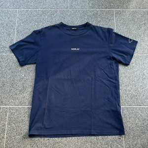 Mörkblå t-shirt från Replay - Snygg mörkblå t-shirt från Replay med klassisk passform och rund hals. T-shirten har diskret Replay-logga broderad på bröstet och är tillverkad i mjuk bomull. Perfekt basic-plagg för en clean och stilren look. 