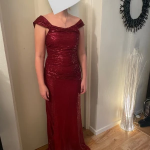 Vinröd glittrig balklänning - Säljer en vinröd balklänning med glittriga paljetter och offshoulder-design. Klänningen har en figurnära passform och är perfekt för bal eller fest. Materialet är syntet med paljett-detaljer som ger en riktigt lyxig känsla. Supersnygg och elegant look!