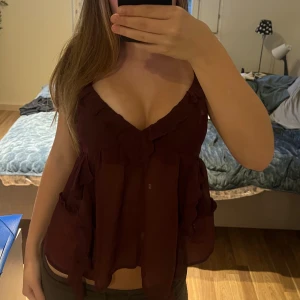 Vinröd fest topp - Säljer en vinröd fest topp med v-ringning och volangdetaljer. Toppen är använd bara en gång så den är i ett jätte bra skick! Säljder denna topp av den enkla anledningen till att inte tycker att den är min stil. 