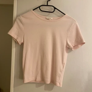 Ljusrosa t-shirt från Gina Tricot - Supersöt ljusrosa t-shirt från Gina Tricot, basically basics-kollektionen. Modellen är croppad med rund hals och korta ärmar. Mjuk och skön material som passar perfekt till jeans eller kjol. Enkel och clean design utan mönster eller detaljer. Finns dock en liten fläck som syns på sista bilden 
