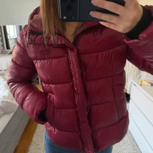 Vinröd pufferjacka från Superdry - Säljer en vinröd pufferjacka från Superdry. Jackan har huva, dragkedja och knappar framtill samt två fickor. Perfekt för kalla dagar och riktigt snygg färg som sticker ut 🤌🏽