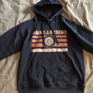 Mörkblå Saint Laurent hoodie med tryck - Snygg mörkblå hoodie från Saint Laurent med huva och snörning. Skick 10/10. Passar 175-185cm!