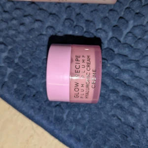 Glow Recipe Plum Plump Hyaluronic Cream - Glow Recipe Plum Plump Hyaluronic Cream i en söt liten rosa burk. Perfekt för att återfukta huden med hyaluronsyra och ge en fräsch känsla. Burken är rund och har en modern design med svart text på framsidan.