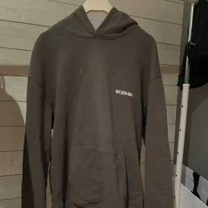 Mörkgrå hoodie med tryck - Säljer en mörkgrå hoodie med texten 'QUÉ SERA SERA' tryckt på bröstet. Perfekt för chill dagar och enkel att matcha med jeans eller joggers. 