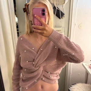 Rosa stickad tröja med pärlor - Superfin ljusrosa stickad tröja med twistad omlottfront och pärldetaljer. Croppad modell med v-ringad hals och långa ärmar. Perfekt för dig som vill ha en mysig men ändå stylish look. Snygg att matcha med jeans eller kjol. Står ej storlek men ungefär xs 🌼