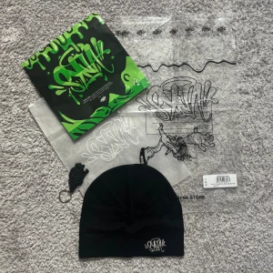 SYNA World Skull Cap - Svart mössa från SYNA med stilrent broderat logotypmärke framtill. Mössan är tillverkad i mjuk polyester och elastan, vilket gör den skön och flexibel. Perfekt för dig som gillar streetstyle och vill ha en clean look med en touch av graffiti.