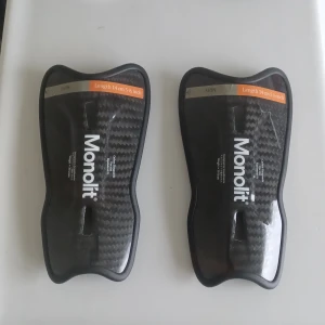 Svarta benskydd Monolit 14 cm - Säljer ett par svarta benskydd från Monolit, längd 14 cm. De har en snygg kolfiberyta och är formade för att sitta bekvämt på smalbenet. Perfekta för fotbollsträning eller match. Lätta och smidiga att använda. Obs aldrig använda.