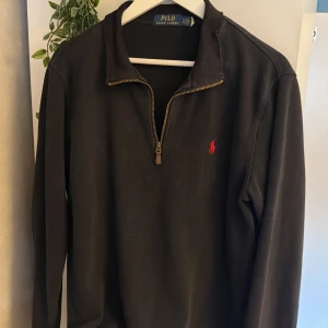Ralph Lauren Halz zip - Svart långärmad tröja från Polo Ralph Lauren med klassisk röd broderad logga på bröstet. Tröjan har en snygg half zip-dragkedja med läderdetalj och hög krage. Perfekt för lager-på-lager och stilren look. Storlek L men passform som M. För referens är jag 180cm, 76kg och den sitter perfekt på mig.
