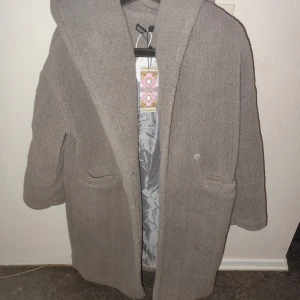 Grå teddyjacka med huva från Boohoo - Mysig grå teddyjacka från Boohoo med oversized passform och stor huva. Jackan har två stora fickor framtill och stängs med knappar. Perfekt för kalla dagar när du vill vara både varm och stilren.  Petite du 34 men inte ett dugg petite uk6