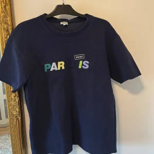 Mörkblå Kenzo t-shirt med tryck - Snygg mörkblå t-shirt från Kenzo med färgglatt 'PARADISE'-tryck på bröstet och Kenzo-logga. Klassisk rund hals och korta ärmar. Skön passform och tillverkad i mjukt bomullstyg. Perfekt för dig som gillar streetstyle och vill sticka ut.