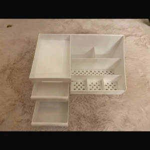 Vit sminkorganiserare med lådor - Praktisk vit sminkorganiserare i plast med tre utdragbara lådor och flera fack i olika storlekar. Perfekt för att hålla ordning på sminkborstar, läppstift, mascara och andra skönhetsprodukter. Mått: 26x16x12 cm. Stilre. OBS den har flera sminkfläckar här och där 