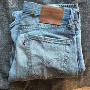 Levi's 501 ljusblå jeans W31 L34 - Ljusblå Levi's 501 Premium jeans med klassisk rak passform och knappgylf. Jeansen har fem fickor och snygga kontrastsömmar. Tillverkade i slitstarkt bomullsmaterial, perfekta för dig som gillar tidlös denimstil. De är använda men har ett gott skick.