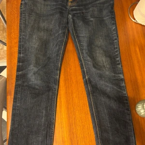 Mörkblå jeans från Nudie Jeans Co - Snygga mörkblå jeans från Nudie Jeans Co med klassisk femficksdesign och kontrastsömmar. Modellen har rak passform och är tillverkad i slitstarkt bomullsjeansmaterial. Perfekt för dig som gillar stilrena och tidlösa jeans. Modell är slim grim Tim. Byxorna är 33 32 men skulle mer säga att det passar någon med 30 30