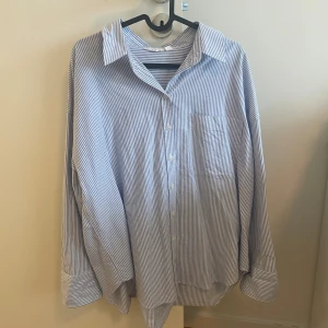 Blåvit randig oversized skjorta - Snygg oversized skjorta med blåvita ränder och klassisk krage. Skjortan har långa ärmar, bröstficka och knäppning framtill.