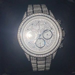 Iced out Dissing silverfärgad klocka med stenar - Säljer en riktigt blingad klocka från Dissing med silverfärgad länk och urtavla täckt av glittrande stenar. Klockan har kronograf-funktion och levereras i originalask med extra länkbitar. Perfekt för dig som vill sticka ut med en lyxig accessoar.