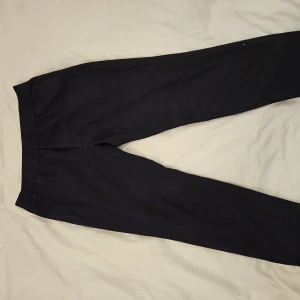 Svarta kostymbyxor från H&M, L - Svarta kostymbyxor från H&M i storlek L. Byxorna har elastisk midja och raka ben med diskreta bakfickor. Perfekta för chill dagar eller när du vill ha det bekvämt. Materialet är mjukt och känns skönt mot huden.